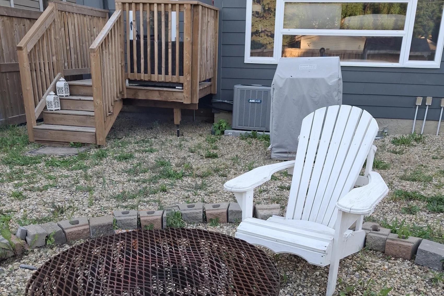 Back yard of the Edmonton house in summer with a fire pit, garden chair and wooden deck