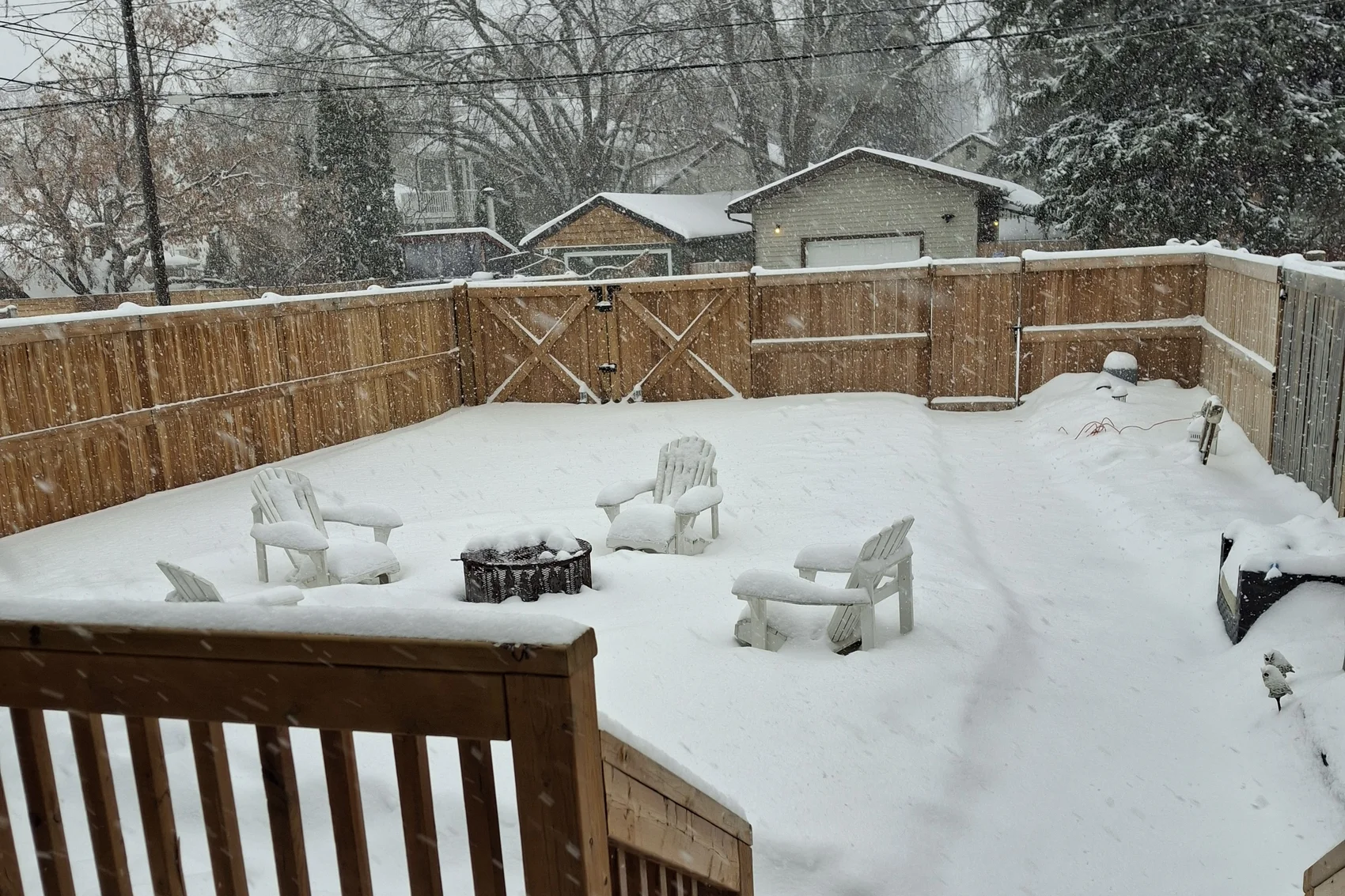 Snow-covered back yard of the house in Edmonton with a fire pit and garden chairs