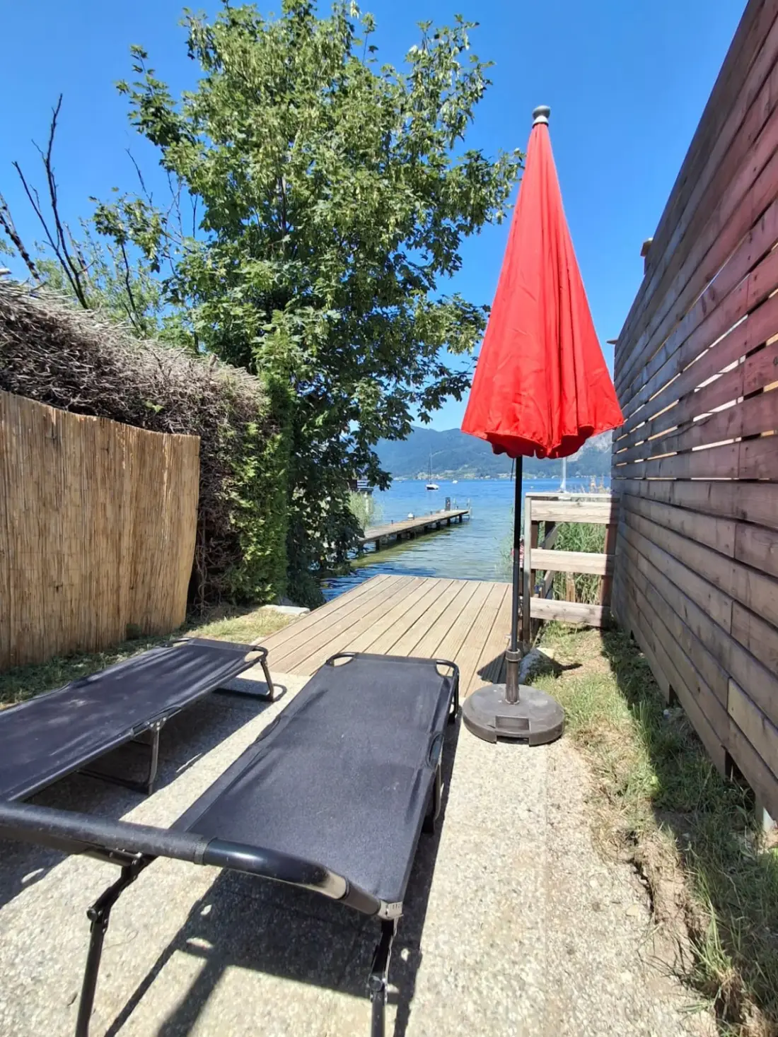 Two sun loungers and a red parasol by the jetty of the lakeside plot