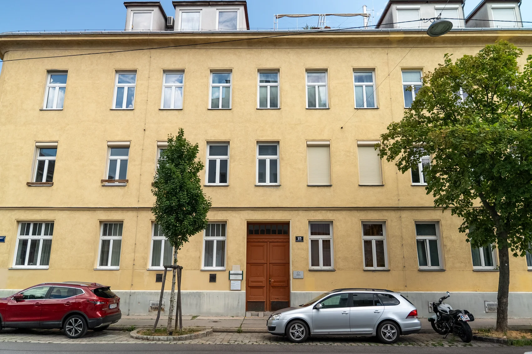 Yellow period facade of Stralehnergasse 15 in Vienna with the entrance and a tree in front